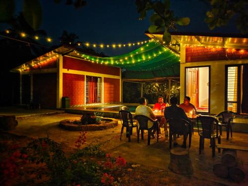 a group of people sitting at a table outside a house at night at Farmhouse with Pool - Kalavady Farmstay in Baindūru