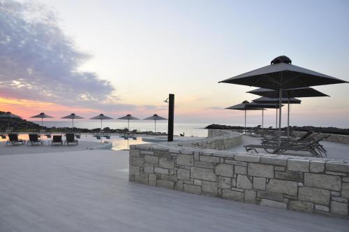 a patio with umbrellas and tables and chairs and the ocean at Kavos Hotel & Suites in Stavros