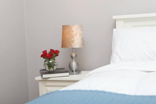 a bed with a table with a lamp and a vase of roses at Foxford penthouse in Foxford