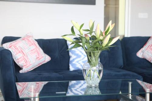a vase with flowers on a glass table with a blue couch at Foxford penthouse in Foxford