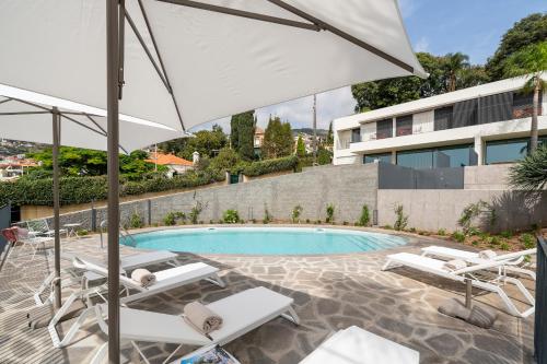 a swimming pool with white chairs and an umbrella at CASA DO MIRADOURO 7 by Heart of Funchal in Funchal
