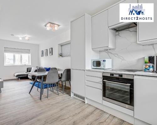 una cocina con armarios blancos y una mesa con sillas. en Modern And Stylish Two Bedroom Apartments by Direct2hosts With Great Location! en Londres