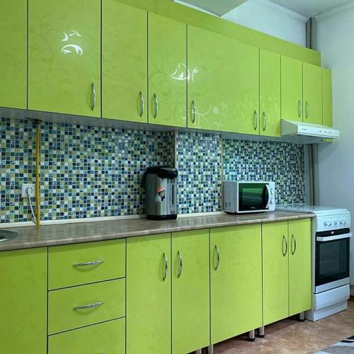 W kuchni znajduje się kuchenka mikrofalowa oraz szafki w odcieniach limonki. w obiekcie Уютная квартира w mieście Taraz