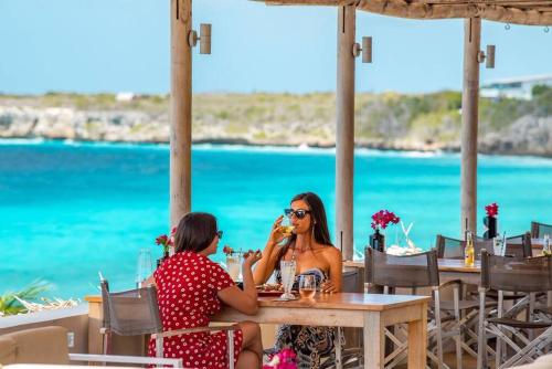 two women sitting at a table on the beach at VillaDelSol-Ocean Front Resort-Pool-up to 8 Guests-Walk to the Beach in Willibrordus