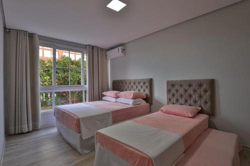two beds in a room with a window at Residencial London AP 104 in Gramado