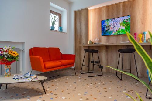 sala de estar con silla naranja y 2 taburetes en Macramè Fazello Rooms, en Sciacca