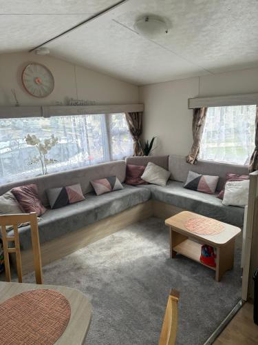 a living room with a couch and a clock at Angie's caravan at Seawick in Saint Osyth