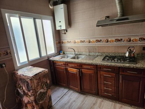 een keuken met houten kasten, een wastafel en een raam bij Tanger méditerranée in Tanger