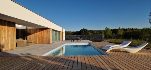 une terrasse avec une piscine et deux chaises blanches dans l'établissement Gleboczek Willa&SPA, à Głęboczek