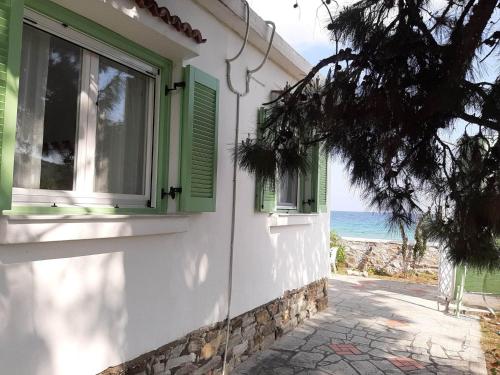 a white house with green shuttered windows and the ocean at House Kokkalas on the beach in Pyrgadikia