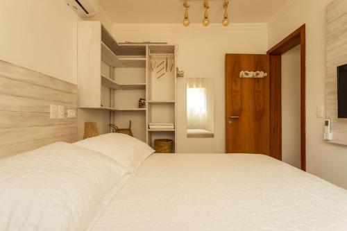 a bedroom with a white bed and a wooden door at Casa d'Aroeira Residencial Boutique - Centro de Juqueí - 2 quadras do mar - Serviço de Praia - Roupa de Cama 600 fios algodão Egípcio - Toalhas Banho e Praia - Tudo Novo - Estacionamento Interno - Cozinha - Consulte unidades com Ofurô Hidro e Cromoterapia in Juquei