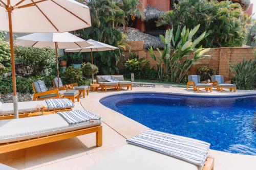 a pool with chairs and umbrellas next to a pool at La Villa Luz (sólo adultos) in Zihuatanejo