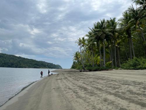 two people walking on a sandy beach with palm trees at hotelsonidosamados-osa in Sierpe