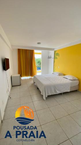 1 dormitorio con cama y pared amarilla en Pousada A Praia, en Parnamirim