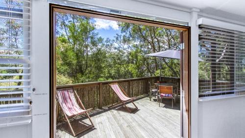 a sliding glass door to a deck with two chairs at Tea Tree House - Pearl Beach in Pearl Beach