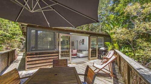 a deck with a table and chairs and an umbrella at Tea Tree House - Pearl Beach in Pearl Beach