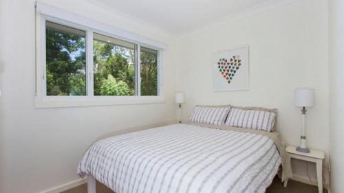 a white bedroom with a bed and a window at Beachworth - Wifi & Pet Friendly in Pearl Beach