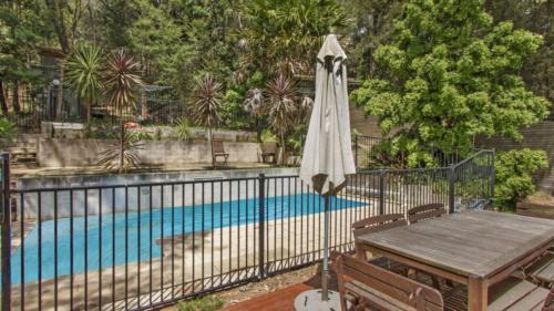 a fence with an umbrella next to a swimming pool at Luxury Escape On Crystal in Pearl Beach