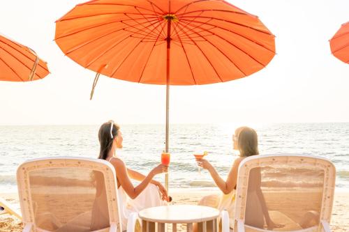 two women sitting at a table under an umbrella on the beach at Bayphere Hotel Pattaya JC in Na Jomtien