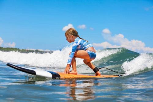 a young girl riding a wave on a surfboard in the ocean at Casa Playa - Modern, Stylish, Spacious, Gated Entry, Rooftop Pool - BEST LOCATION - 4 BLKS to Ocean Avenue in Los Angeles