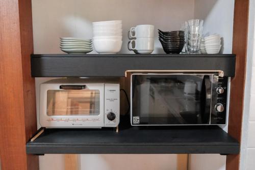 a microwave on a shelf with plates and bowls at ARUYOguesthouse 一棟貸切 大人数でbbqと焚き火を楽しむ in Haibara
