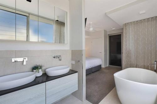 - Baño con 2 lavabos, bañera y cama en Elysee Beachside Apartments Alexandra Headland, en Alexandra Headland