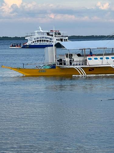 a yellow boat in the water with a cruise ship at 5 Min Walk To Famous Blue Water Resort And Tourist Area in Maribago