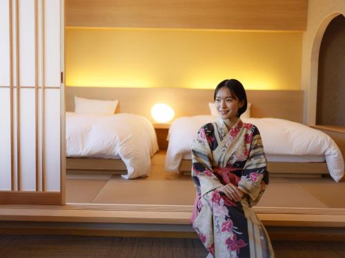 a woman in a kimono standing in a room with beds at Ohashikan in Matsue