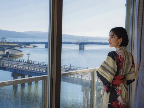 a woman standing in a window looking out at the water at Ohashikan in Matsue