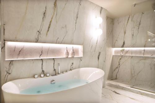 a white bathroom with a tub and a shower at Mirabello Bay Luxury Resort in Agios Nikolaos