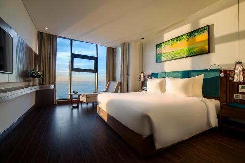 ein Hotelzimmer mit einem großen Bett und einem großen Fenster in der Unterkunft Maximilan Danang Beach Hotel in Đà Nẵng