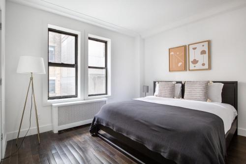 a white bedroom with a large bed and two windows at Midtown 2br w doorman wd nr Central Park NYC-1144 in New York