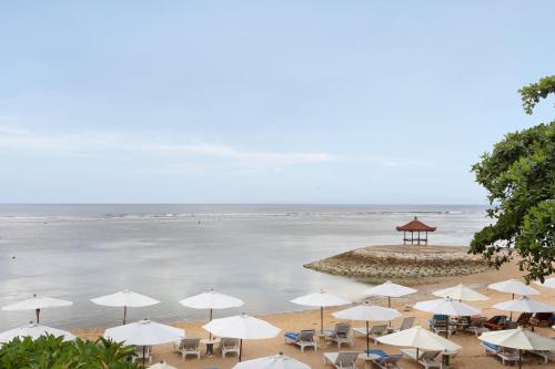 a beach with white umbrellas and chairs and the ocean at Respati Beach Hotel in Sanur