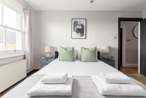 a white bedroom with a large bed with green pillows at The Notting Hill Apartment in London
