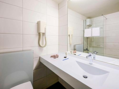 ein weißes Badezimmer mit einem Waschbecken und einem Spiegel in der Unterkunft ibis Zurich Adliswil in Zürich