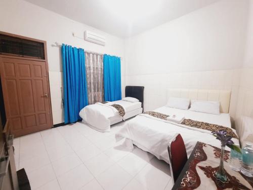 two beds in a room with blue curtains at Hotel Meurah Mulia Syariah in Banda Aceh