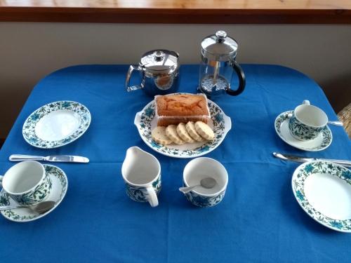 uma mesa com uma toalha de mesa azul com um bolo e chávenas em Bridge of Bennie Cottage em Banchory