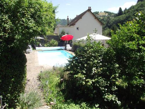 een zwembad met een rode parasol naast een huis bij Vue du Pont in Entraygues-sur-Truyère