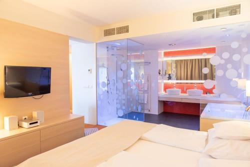 a bedroom with a bed and a tv and a bathroom at Kolping Family Resort in Hévíz