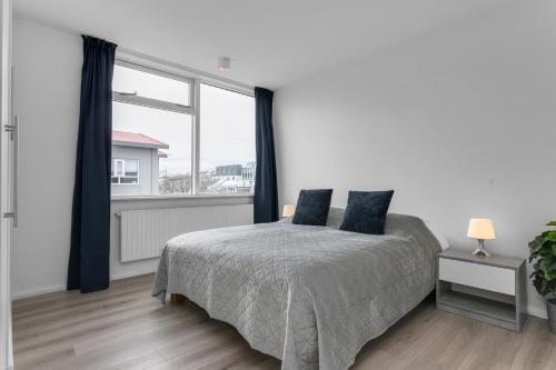a white bedroom with a bed and a large window at GreenKey Apartment V13 in Reykjavík