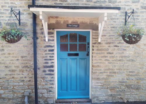 Cotswold Cottage Bed & Breakfast في Luckington: الباب الأزرق على مبنى من الطوب مع اثنين من النباتات الفخارية