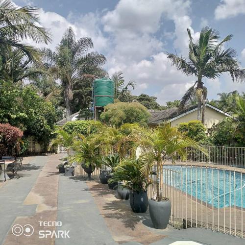 a swimming pool with palm trees and a fence at Guesthouse with green garden and pool - 2102 in Harare