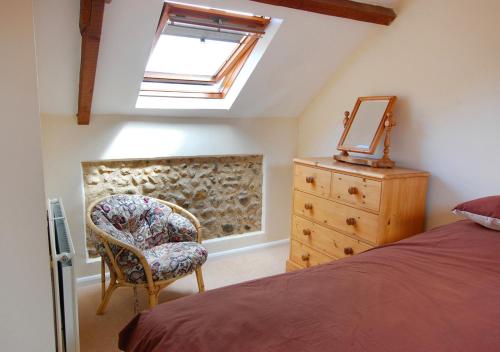 um quarto com uma cama, uma cadeira e uma cómoda em Church Barn Cottage em Saxlingham