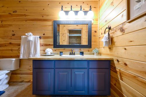 uma casa de banho com um lavatório azul e um espelho. em Hickory Bear - Cabin surrounded by pines, Sleeps 10, Hot Tub, Fire Pit, Arcade, Foosball Table & Deck Slide em Broken Bow