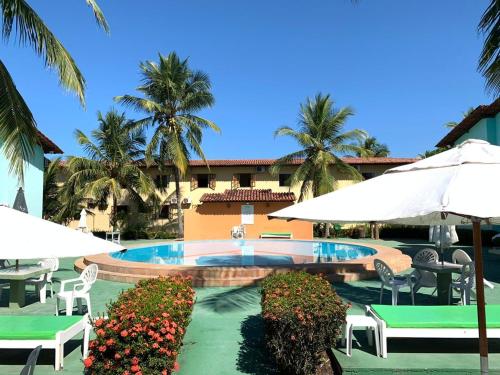 una piscina con sillas y sombrillas y un edificio en Apto no condomínio Taperapuan Village, en Porto Seguro