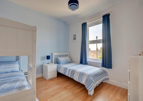 a bedroom with a bed and a window with blue curtains at Beachcomber Cottage in Hunstanton