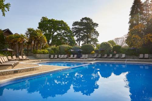 a large swimming pool with chairs and trees at Macdonald Elmers Court Resort in Lymington