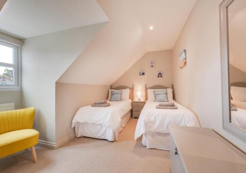 a attic bedroom with two beds and a yellow chair at Curlew Cottage in Wells next the Sea