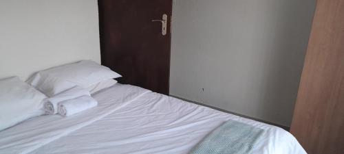 a bed with white sheets and pillows in a room at Dawn Park Guest House in Boksburg