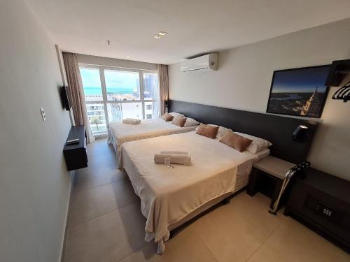 a hotel room with two beds and a large window at Lindos Flats Studios no Qualité in João Pessoa